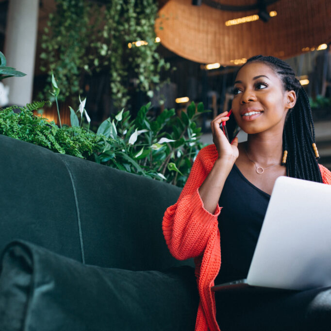 African american woman with phone and laptop in a cafe
